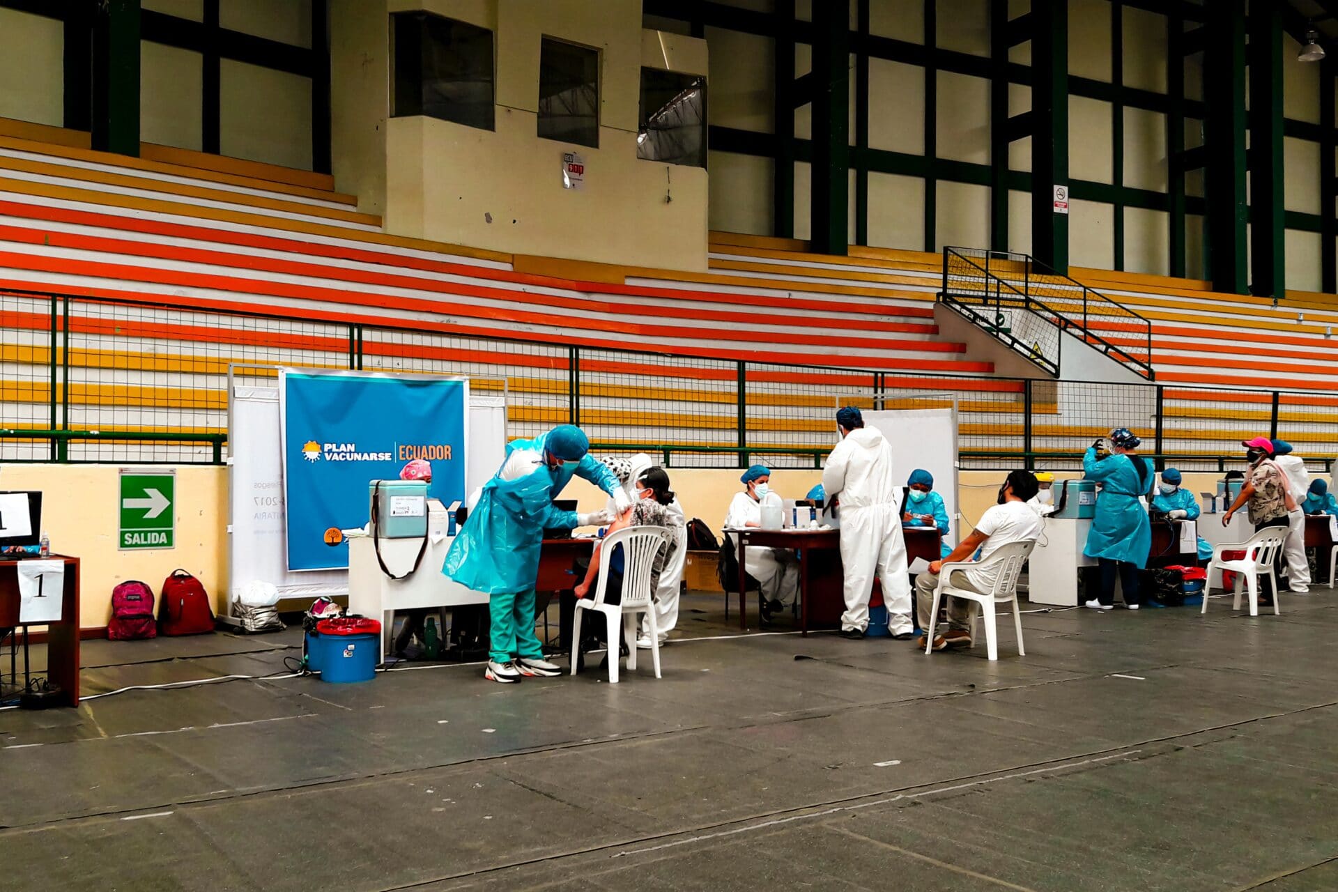 A roll of people sitting down in an arena to receive a needle from a nurse