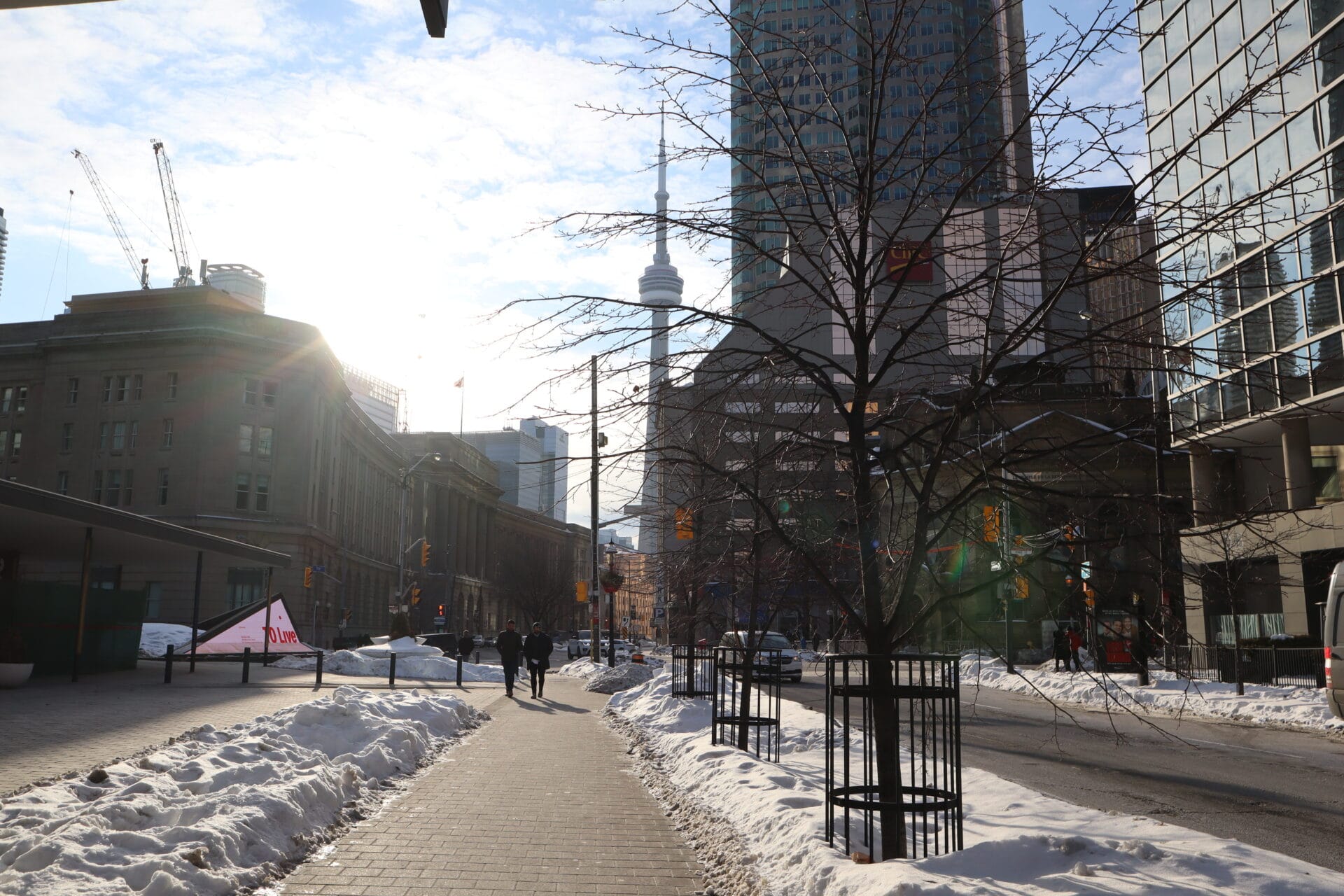 Two men are walking towards the camera, with snow on the sides of the sidewalk.