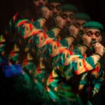 Siddartha holds a microphone, looking to his side as he performs. The image is overlayed with lower opacity copies of Siddartha.